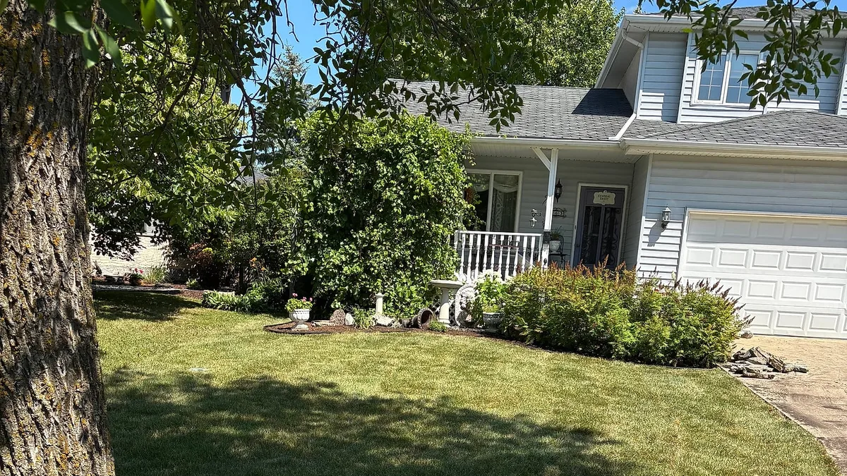 Freshly cut lawn under a mature tree in front of a Winnipeg home